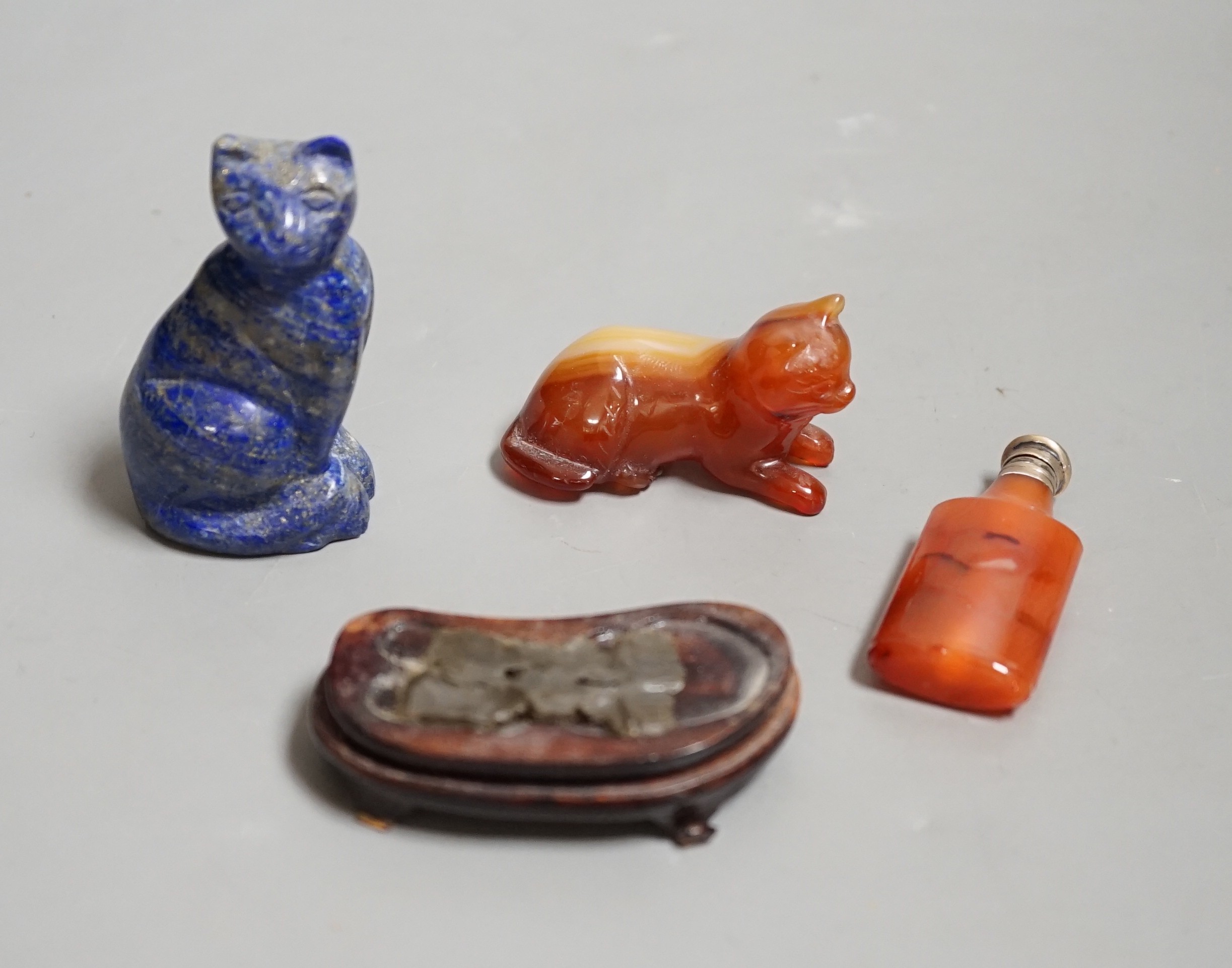 A Chinese carved lapis lazuli seated cat, a banded agate recumbent cat on hardwood stand and a white metal mounted agate scent bottle